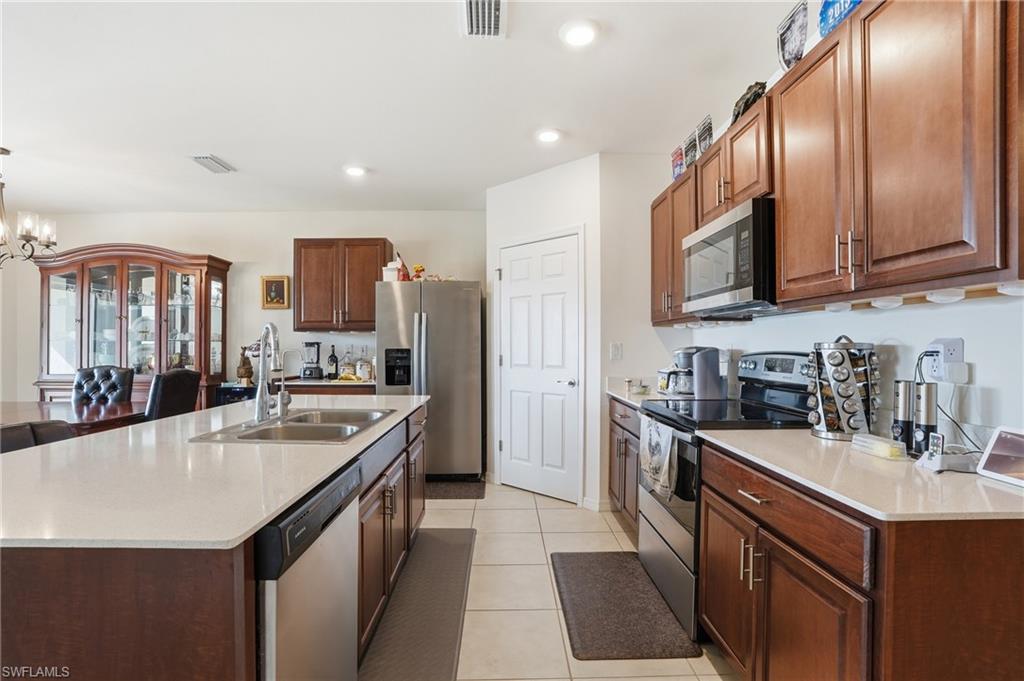 Kitchen featuring stainless steel appliances, an island with sink, suspended lighting, light tile patterned floors, and light stone countertops