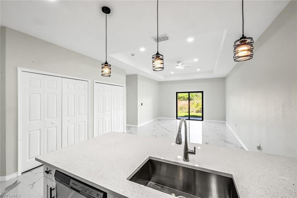 Kitchen featuring light stone countertops, stainless steel dishwasher, light marble finish floors, and a raised ceiling