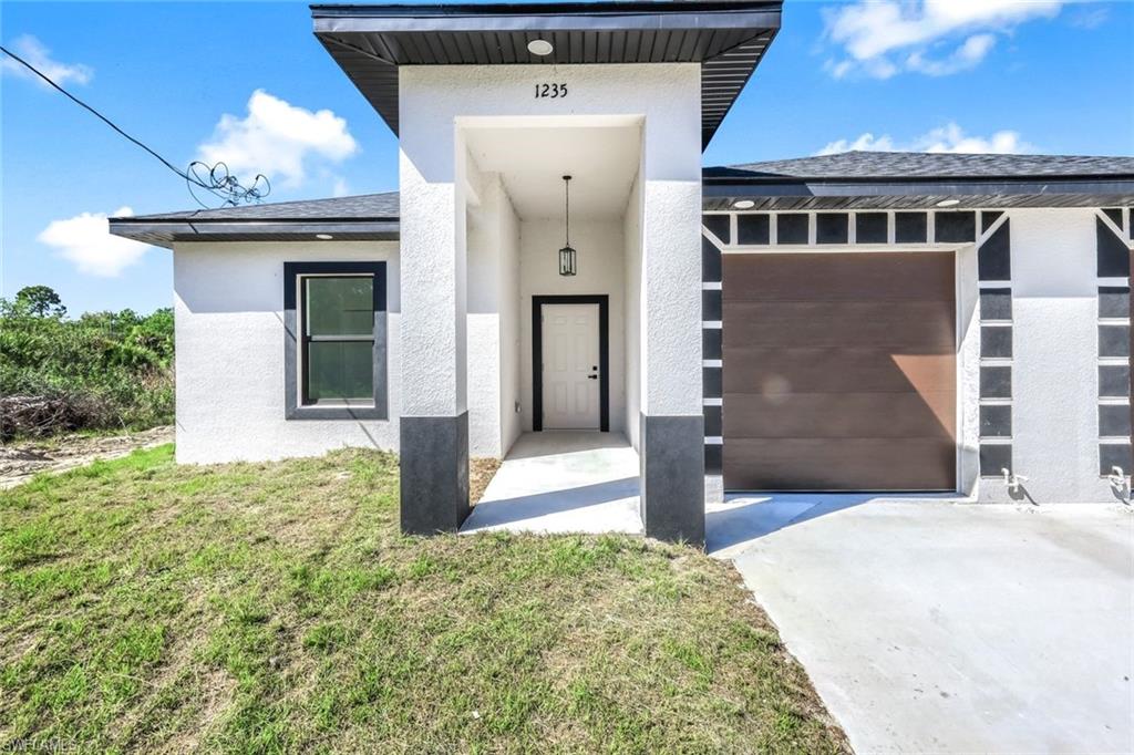 View of front of property with an attached garage, stucco siding, a front lawn, and driveway