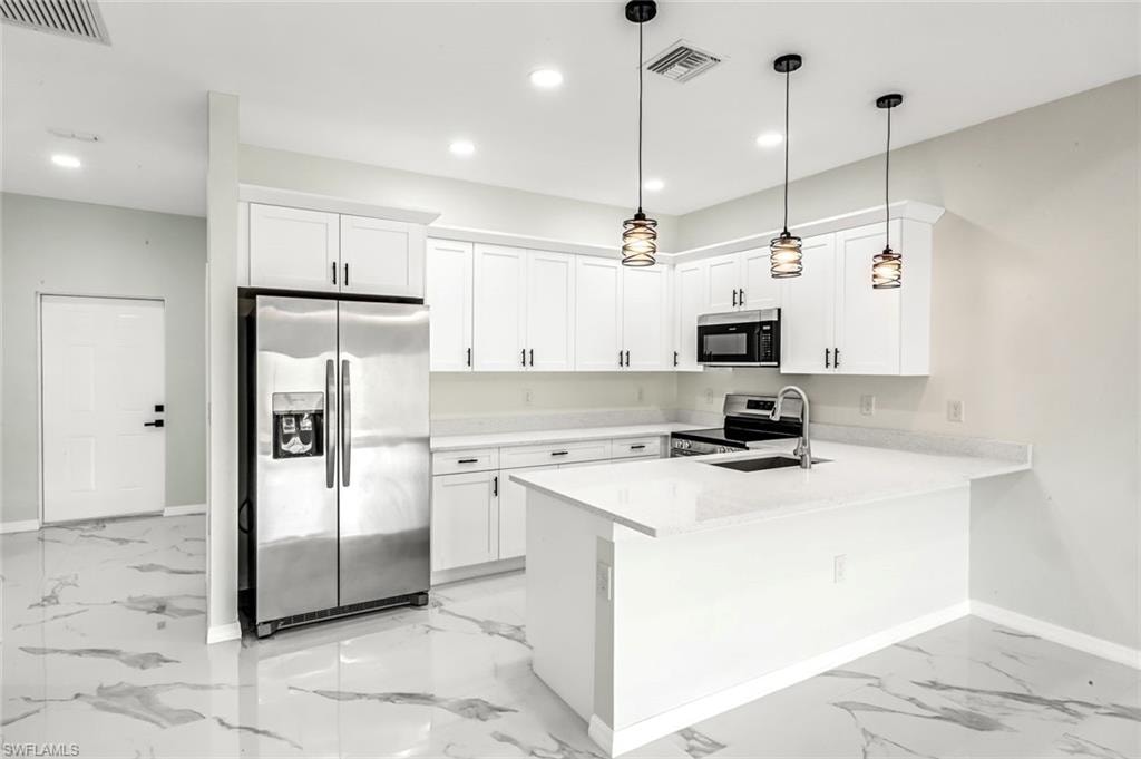 Kitchen with stainless steel appliances, white cabinets, a peninsula, and light stone countertops