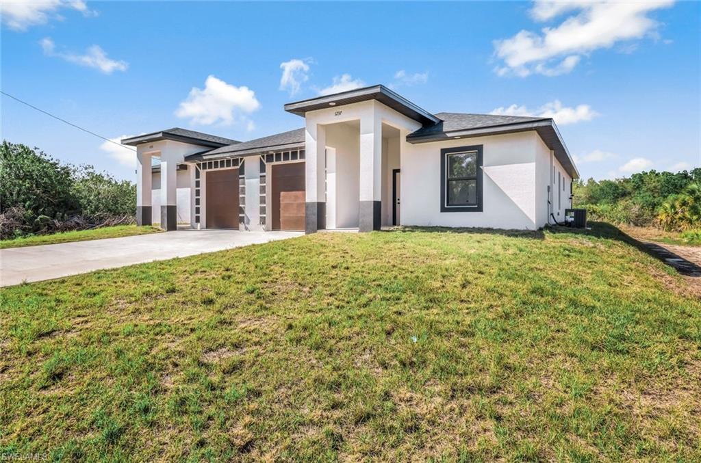 Prairie-style home with an attached garage, driveway, a front yard, and stucco siding