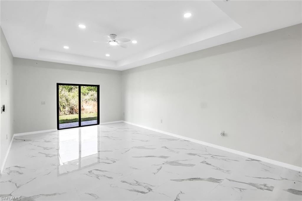 Unfurnished room with recessed lighting, a ceiling fan, light marble finish floors, and a tray ceiling