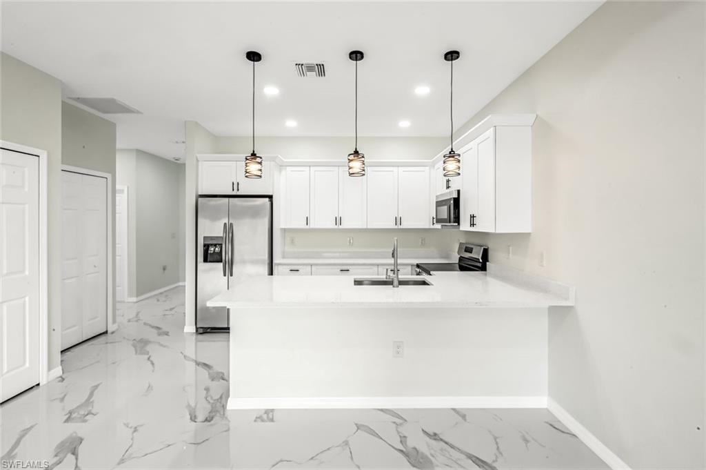 Kitchen featuring a peninsula, stainless steel appliances, white cabinetry, light stone counters, and decorative light fixtures