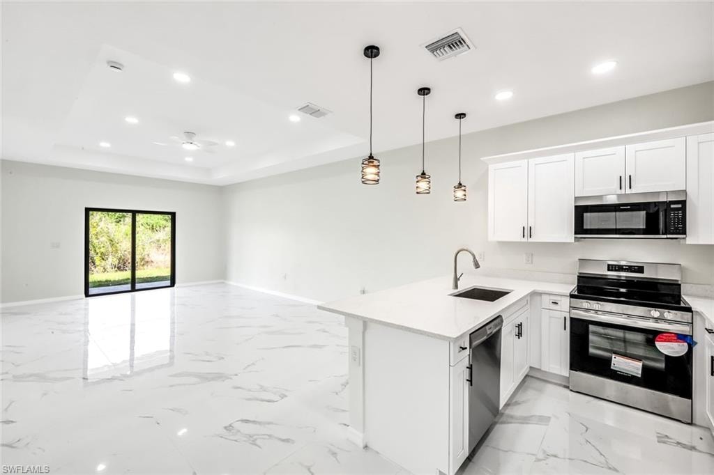 Kitchen featuring stainless steel appliances, white cabinets, open floor plan, a peninsula, and light stone countertops