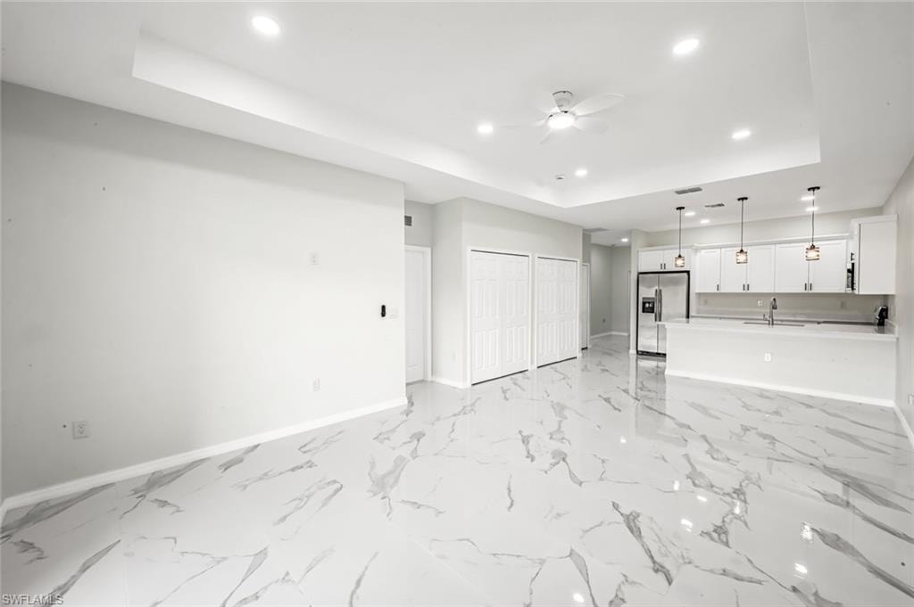 Unfurnished living room featuring a tray ceiling, ceiling fan, and recessed lighting