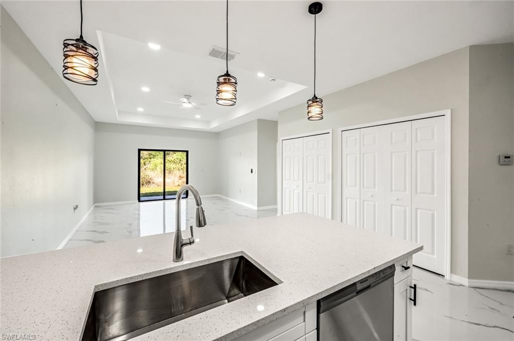 Kitchen with dishwasher, light stone counters, light marble finish floors, open floor plan, and hanging light fixtures