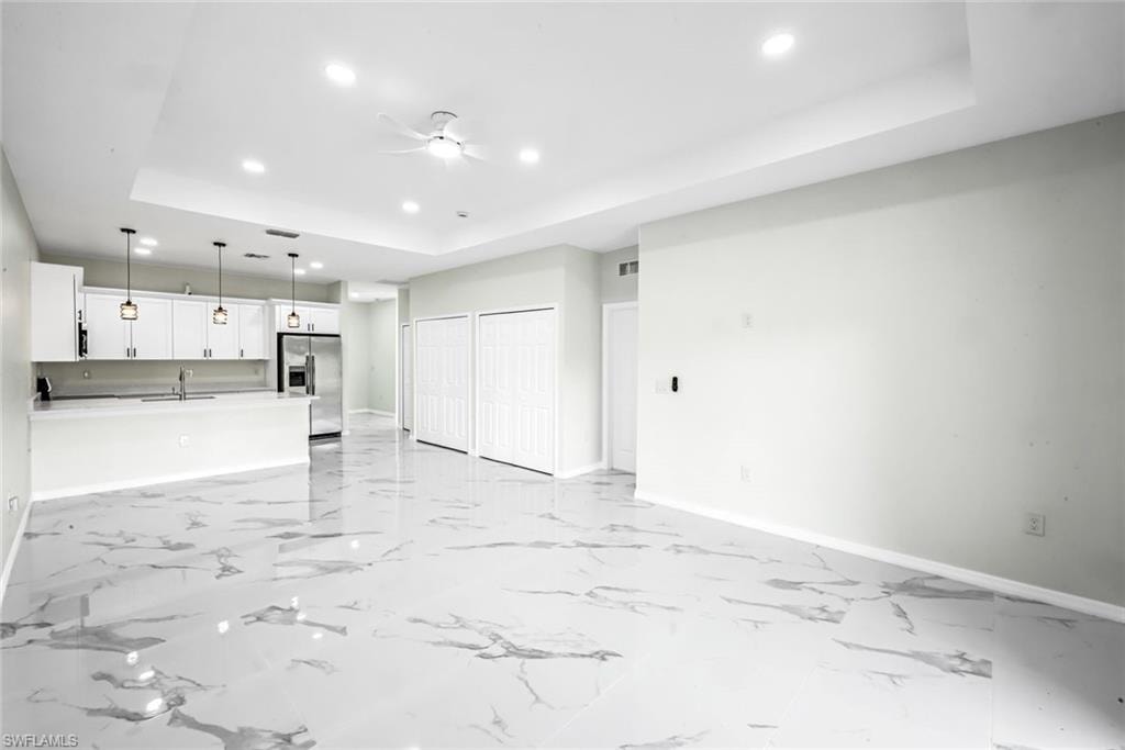 Unfurnished living room featuring a raised ceiling, recessed lighting, and ceiling fan