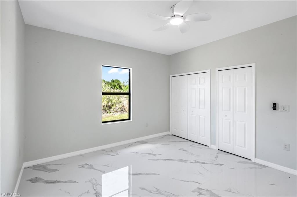 Unfurnished bedroom featuring multiple closets, a ceiling fan, and light marble finish flooring
