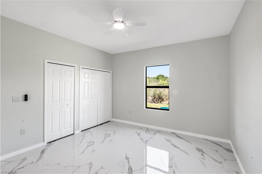 Unfurnished bedroom featuring two closets, ceiling fan, and light marble finish floors