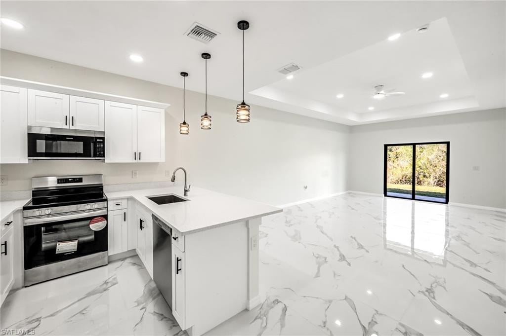 Kitchen featuring stainless steel appliances, open floor plan, a peninsula, white cabinetry, and a raised ceiling