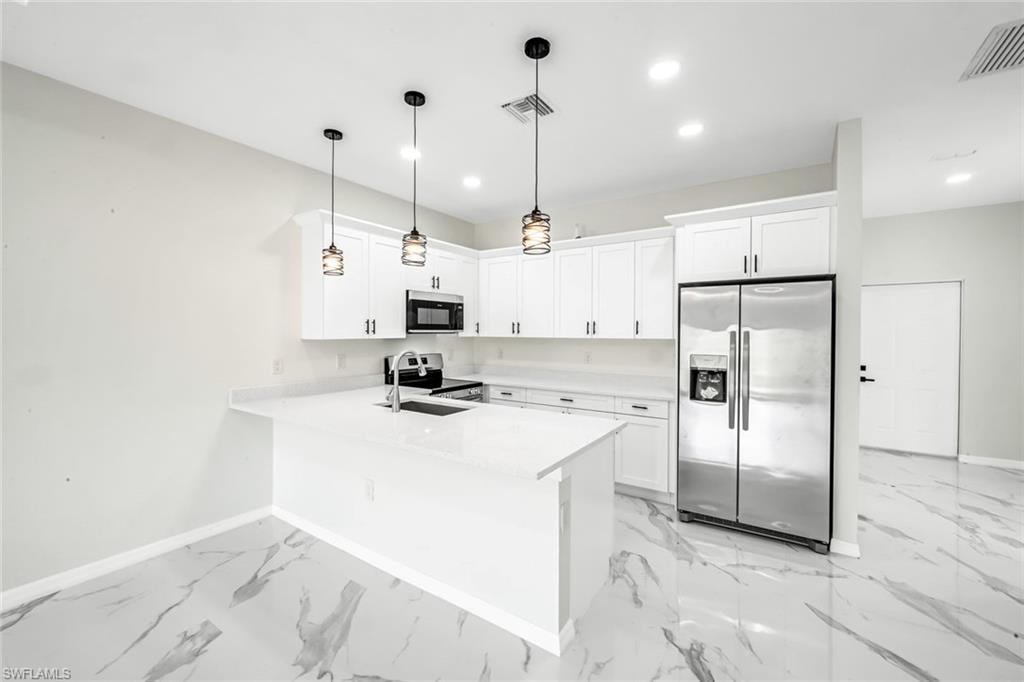 Kitchen with stainless steel appliances, white cabinets, a peninsula, decorative light fixtures, and light stone countertops