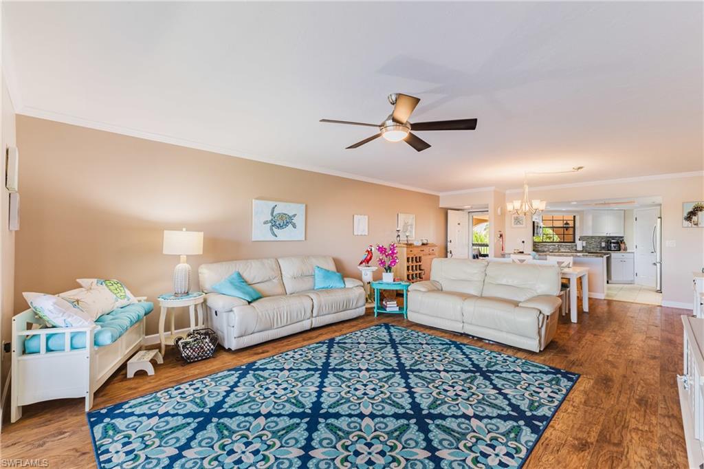 Living area featuring crown molding, ceiling fan, dark wood finished floors, and a chandelier