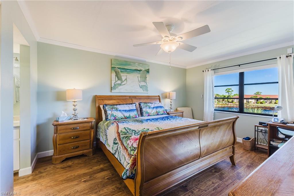 Master bedroom featuring dark wood-style floors, crown molding, a ceiling fan, connected bathroom, and a water view