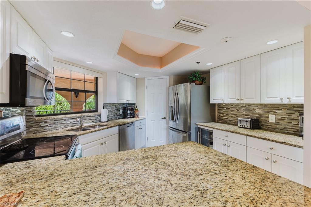 Kitchen with a raised ceiling, light stone counters, stainless steel appliances, white cabinets, and decorative backsplash