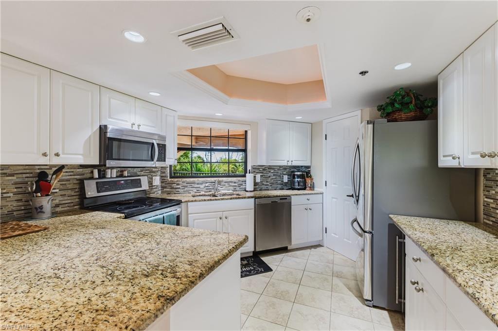 Kitchen featuring a raised ceiling, stainless steel appliances, white cabinetry, light stone countertops, and tasteful backsplash