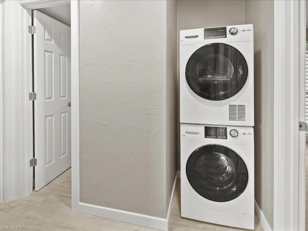 Laundry area with a textured wall, light wood finished floors, and stacked washer and clothes dryer