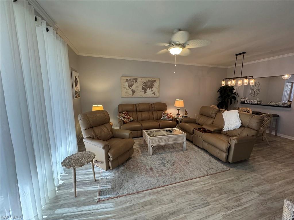 Living room featuring ornamental molding, wood-type flooring, and ceiling fan with notable chandelier