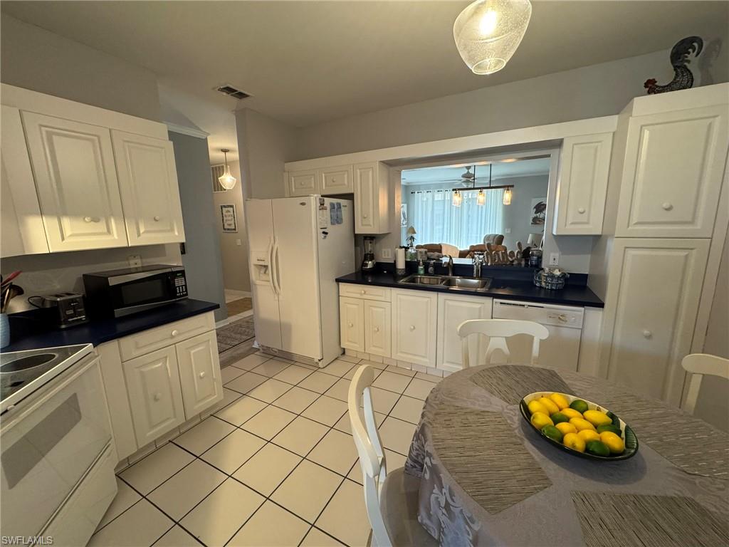 Kitchen featuring white cabinets, sink, light tile patterned floors, and white appliances