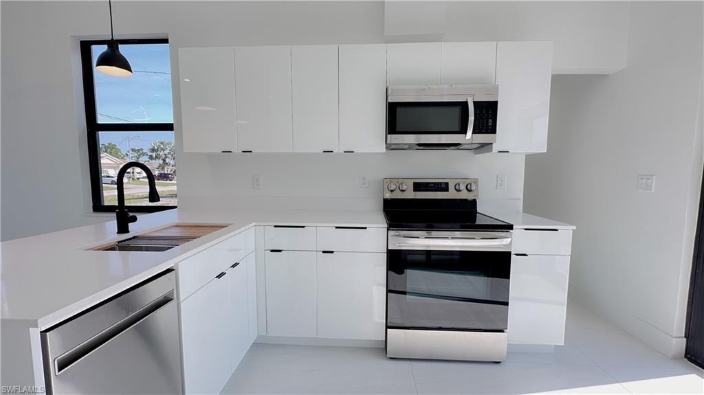 Kitchen with stainless steel appliances, white cabinetry, modern cabinets, and decorative light fixtures