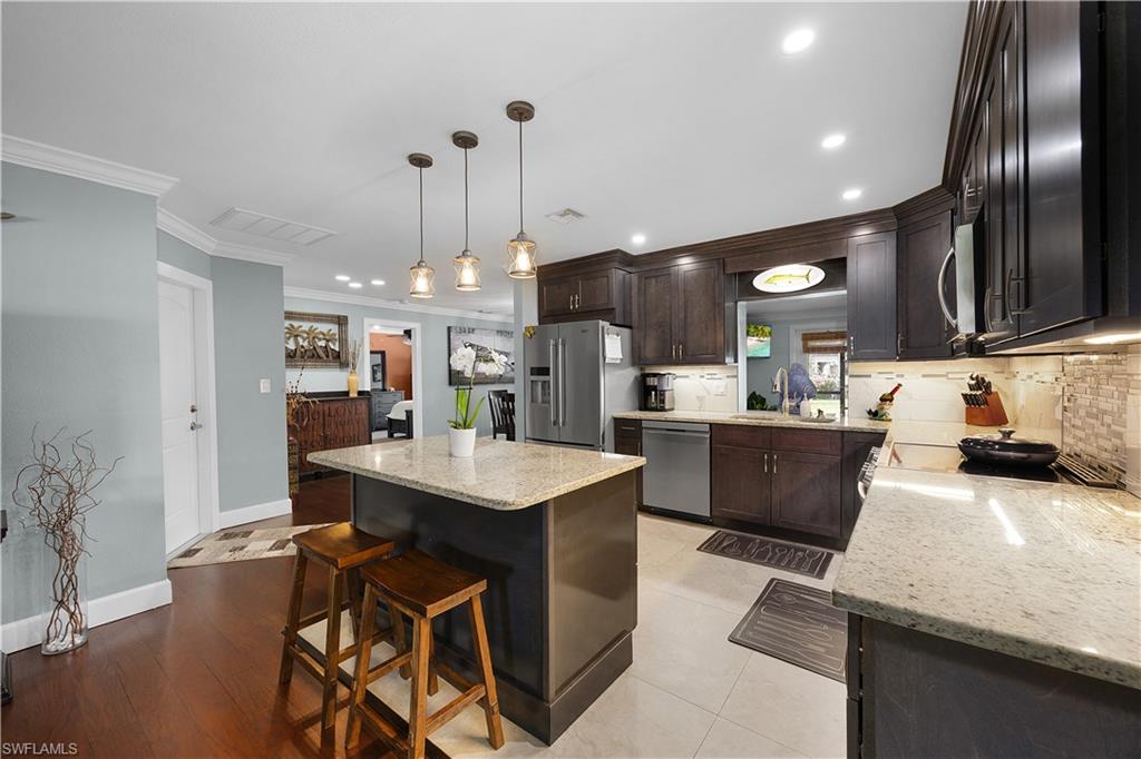 Kitchen with a breakfast bar, ornamental molding, light stone counters, dark wood finish cabinets, and stainless steel appliances