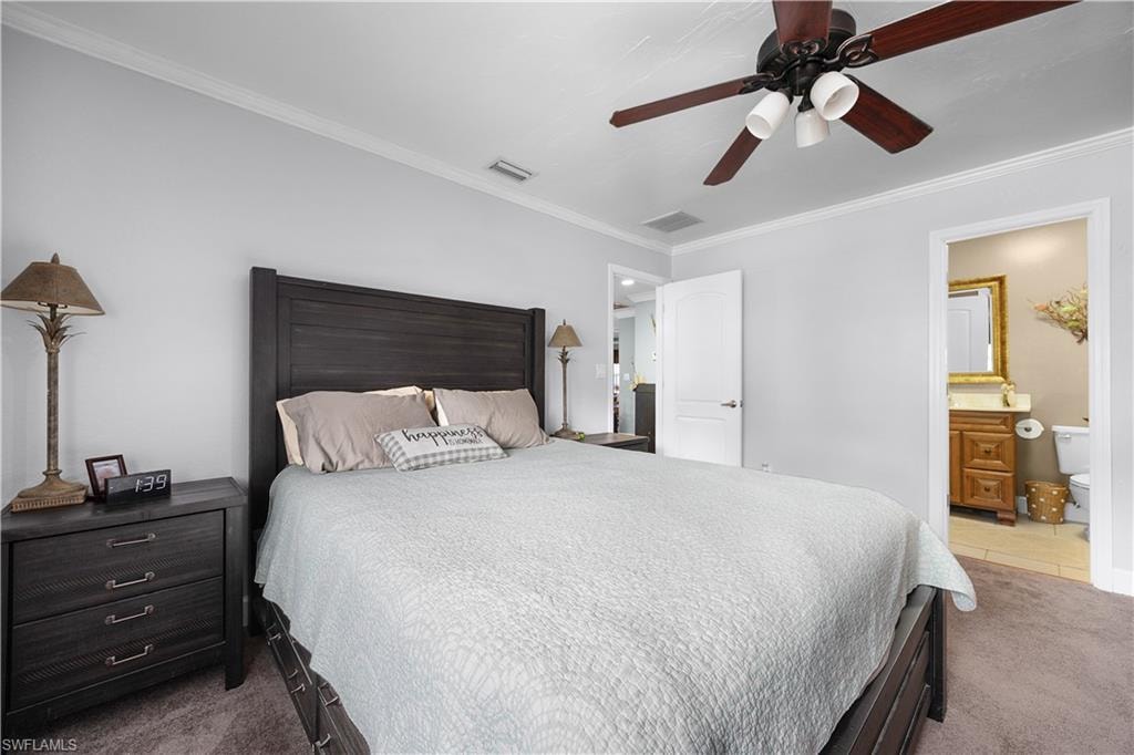 Bedroom with light carpet, ornamental molding, ensuite bath, and a ceiling fan