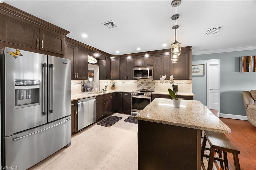 Kitchen with stainless steel appliances, light stone counters, a center island, tasteful backsplash, and crown molding