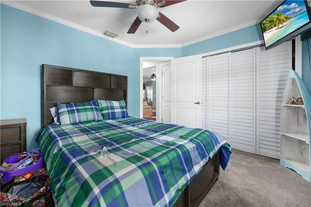 Carpeted bedroom featuring ornamental molding, a closet, and a ceiling fan