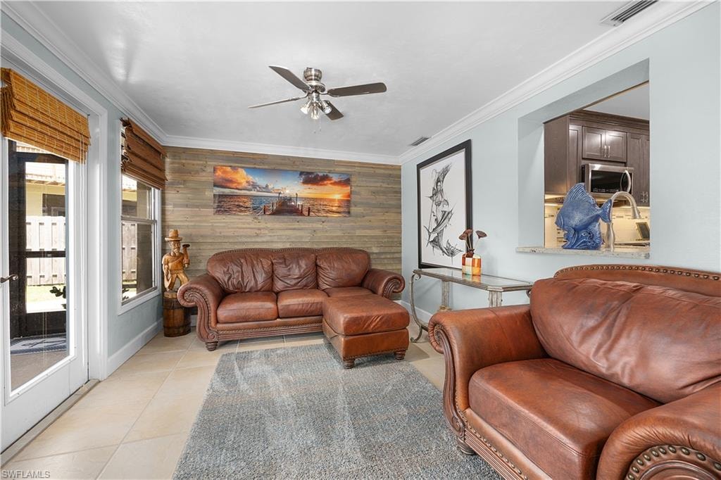 Living room with a ceiling fan, ornamental molding, wood walls, and light tile patterned floors