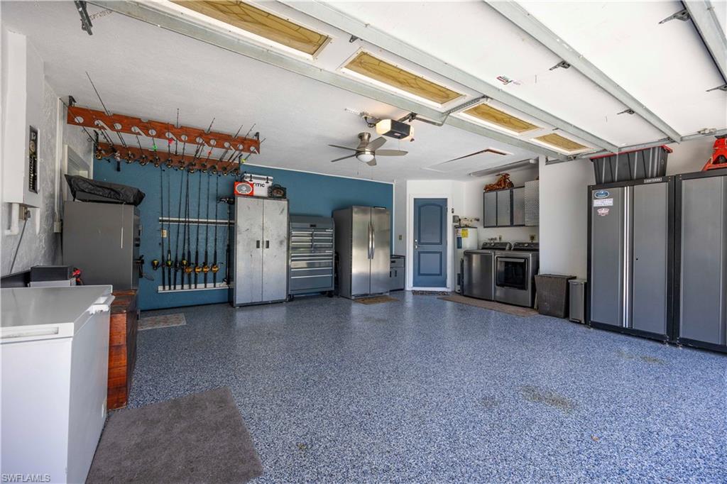 Garage featuring freestanding refrigerator, a ceiling fan, washer and clothes dryer, electric panel, and electric water heater