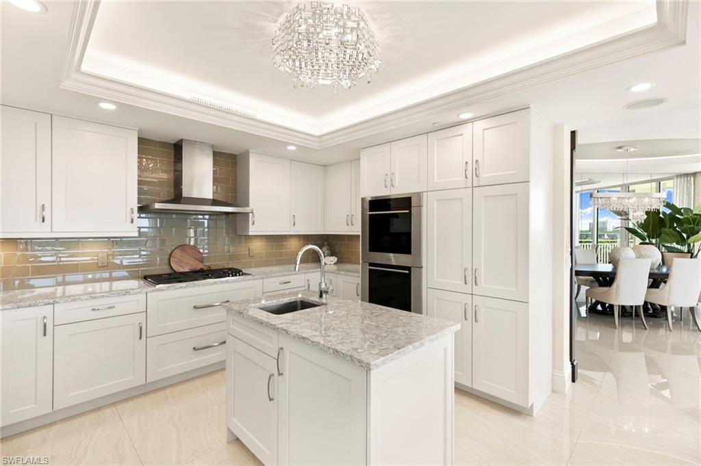 Another view of Kitchen featuring a raised ceiling, an island with sink, white cabinetry