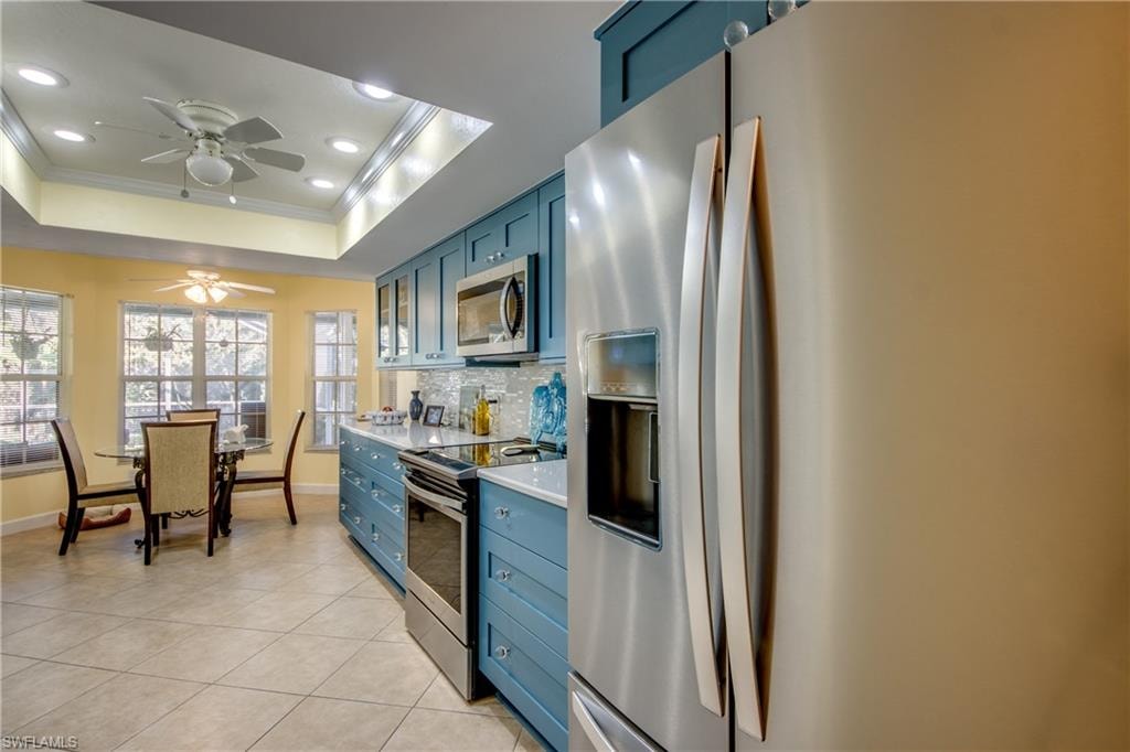 Kitchen with ornamental molding, stainless steel appliances, a tray ceiling, ceiling fan, and blue cabinetry