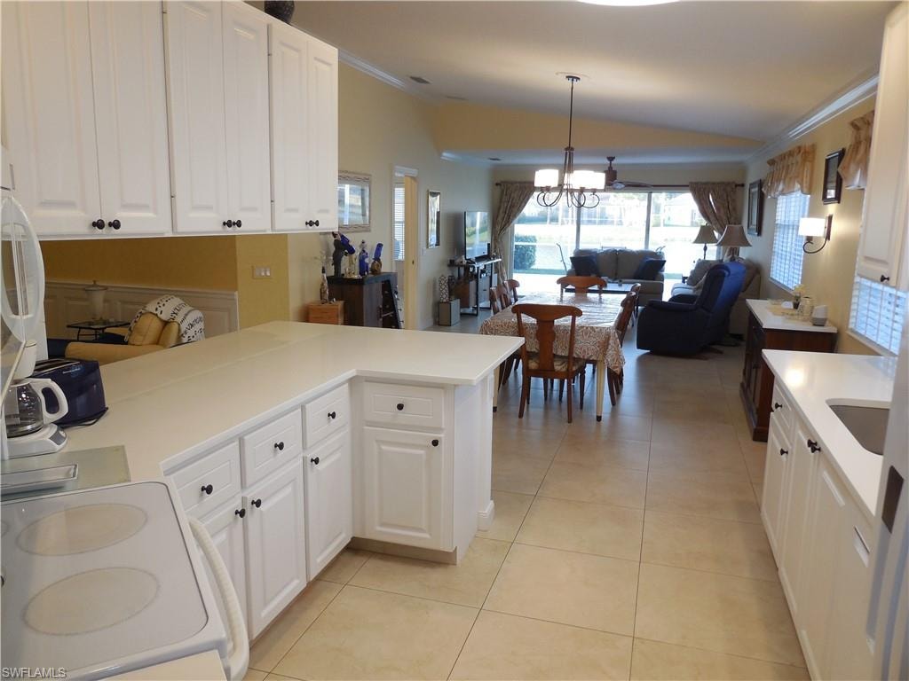 Kitchen with kitchen peninsula, light tile patterned floors, pendant lighting, white cabinetry, and an inviting chandelier