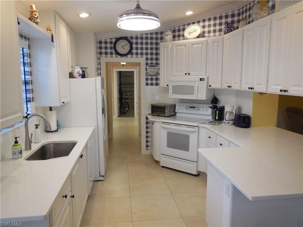 Kitchen featuring white appliances, white cabinets, decorative light fixtures, and sink