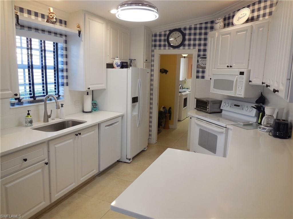 Kitchen with sink, white cabinetry, white appliances, ornamental molding, and washer / dryer