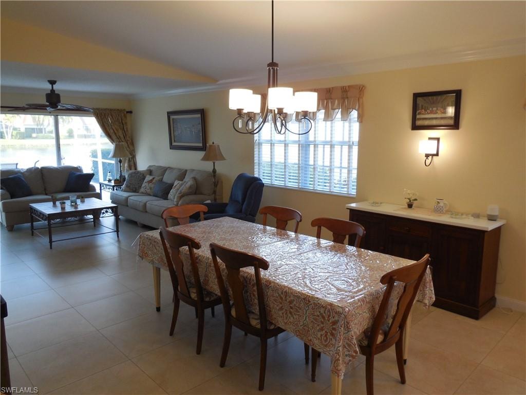Tiled dining space with ceiling fan with notable chandelier, ornamental molding, vaulted ceiling, and a healthy amount of sunlight