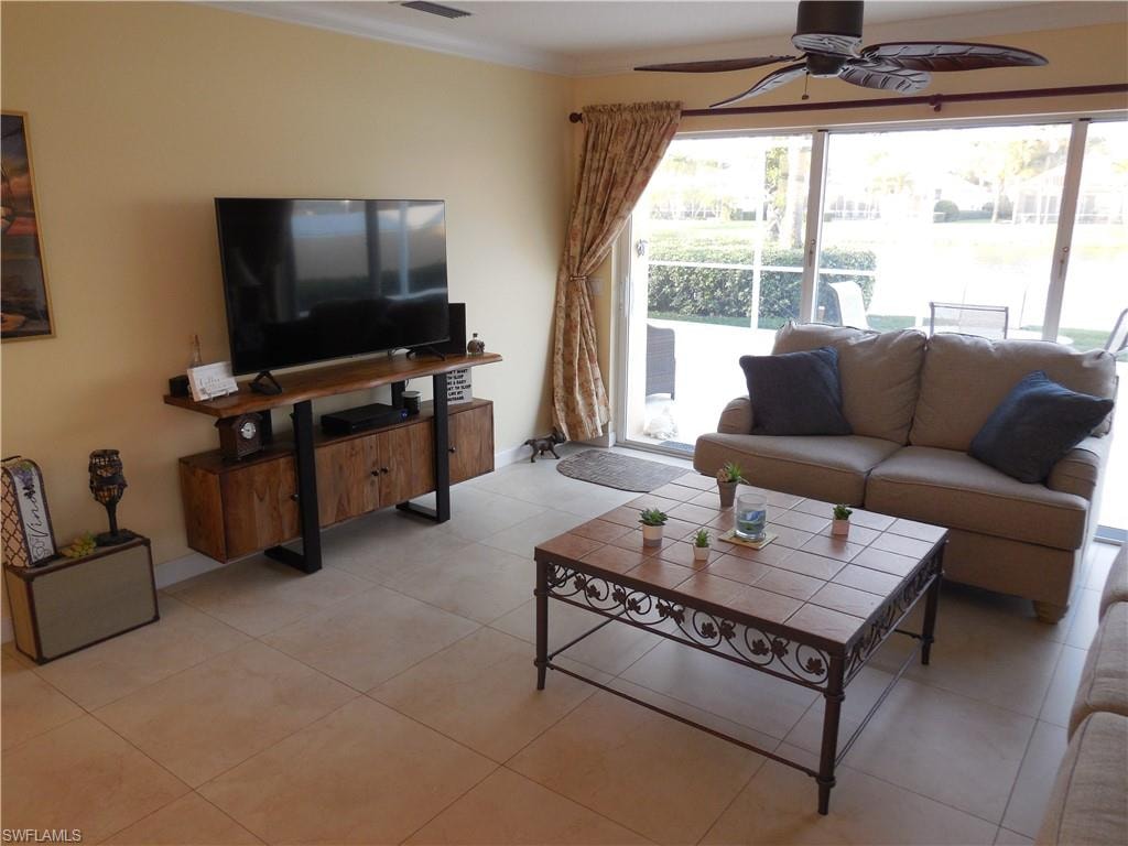 Living room featuring ceiling fan, ornamental molding, and light tile patterned floors