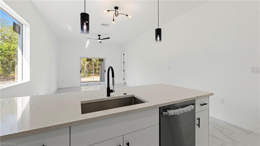 Kitchen featuring white cabinets, dishwasher, light stone counters, and hanging light fixtures