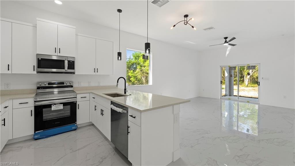 Kitchen with stainless steel appliances, light marble finish flooring, a peninsula, and white cabinetry