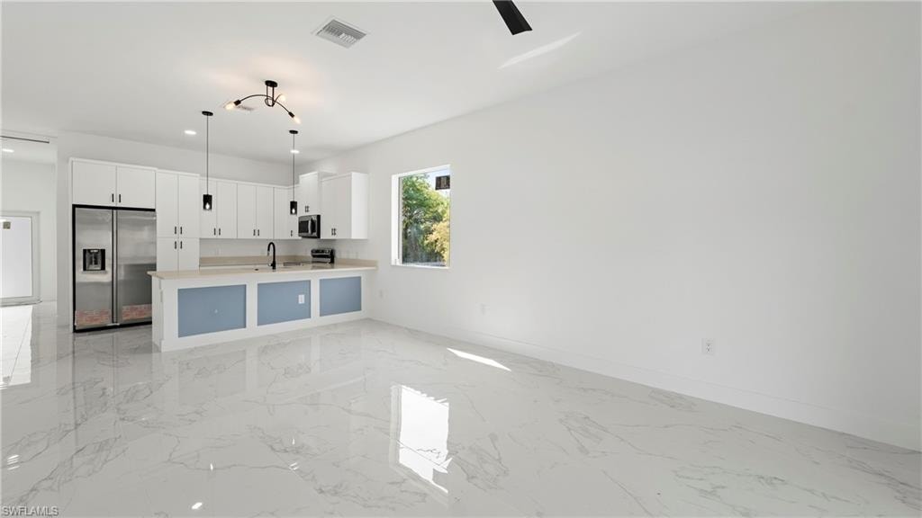Kitchen featuring white cabinets, stainless steel appliances, open floor plan, pendant lighting, and a peninsula