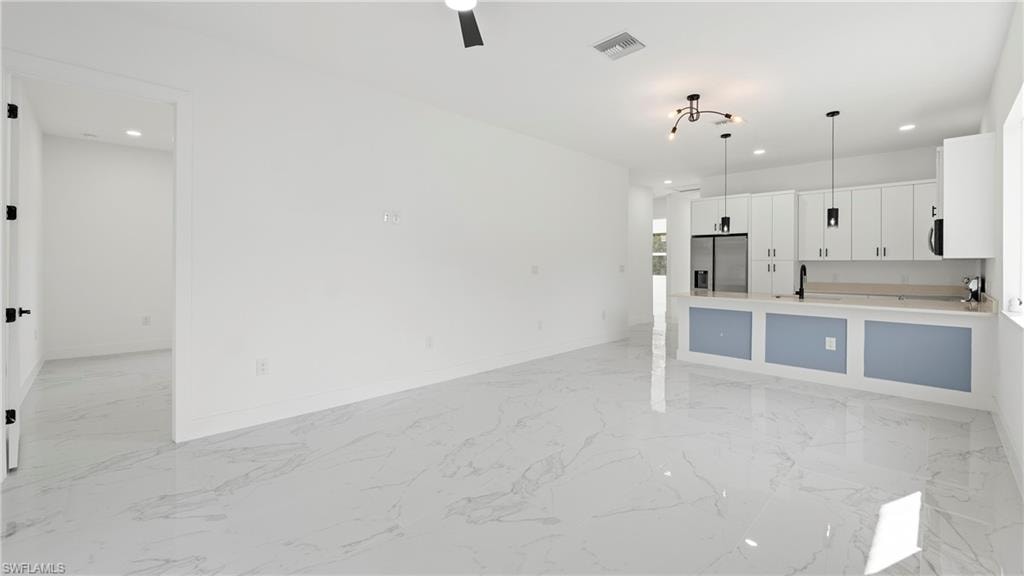 Kitchen with white cabinets, hanging light fixtures, stainless steel refrigerator with ice dispenser, open floor plan, and light marble finish floors