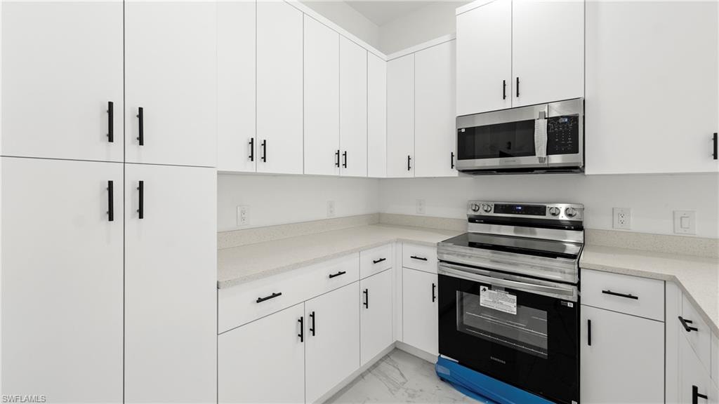 Kitchen featuring stainless steel appliances, white cabinetry, light marble finish floors, and light stone countertops