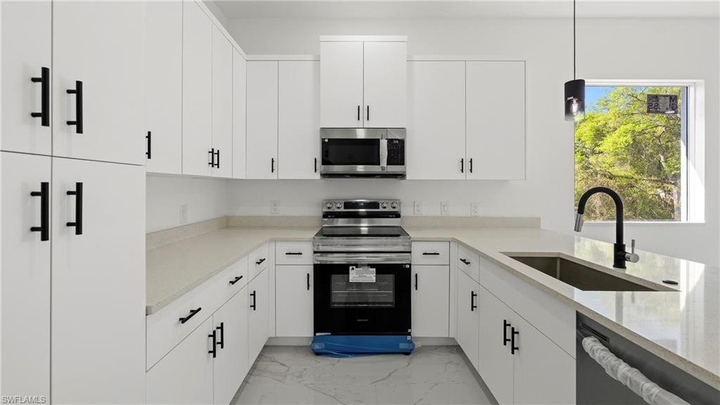 Kitchen with stainless steel appliances, white cabinetry, hanging light fixtures, and light stone counters
