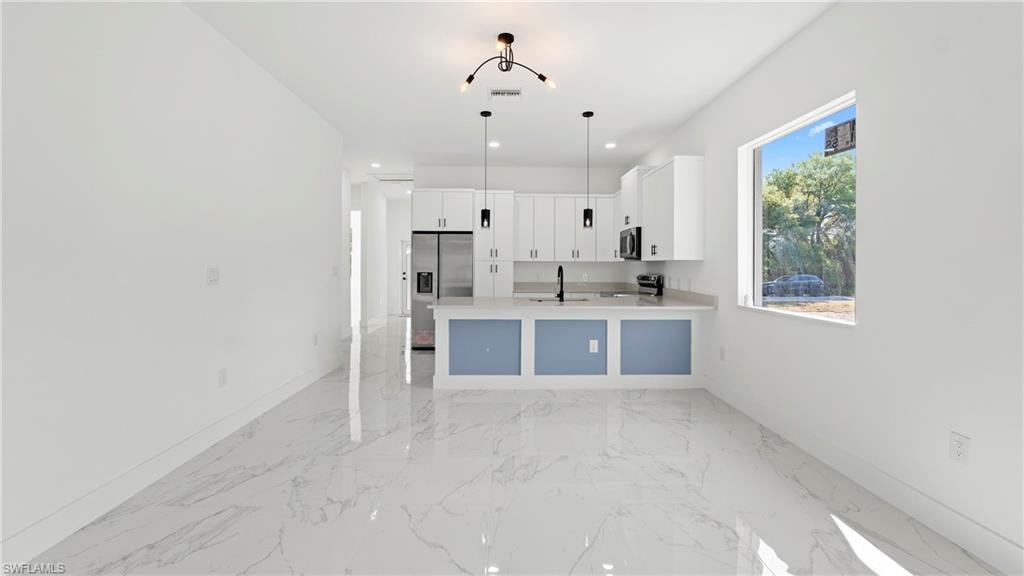 Kitchen featuring white cabinetry, pendant lighting, a peninsula, stainless steel appliances, and open floor plan