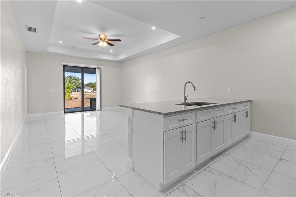 Kitchen featuring light stone countertops, a peninsula, a ceiling fan, light marble finish floors, and open floor plan