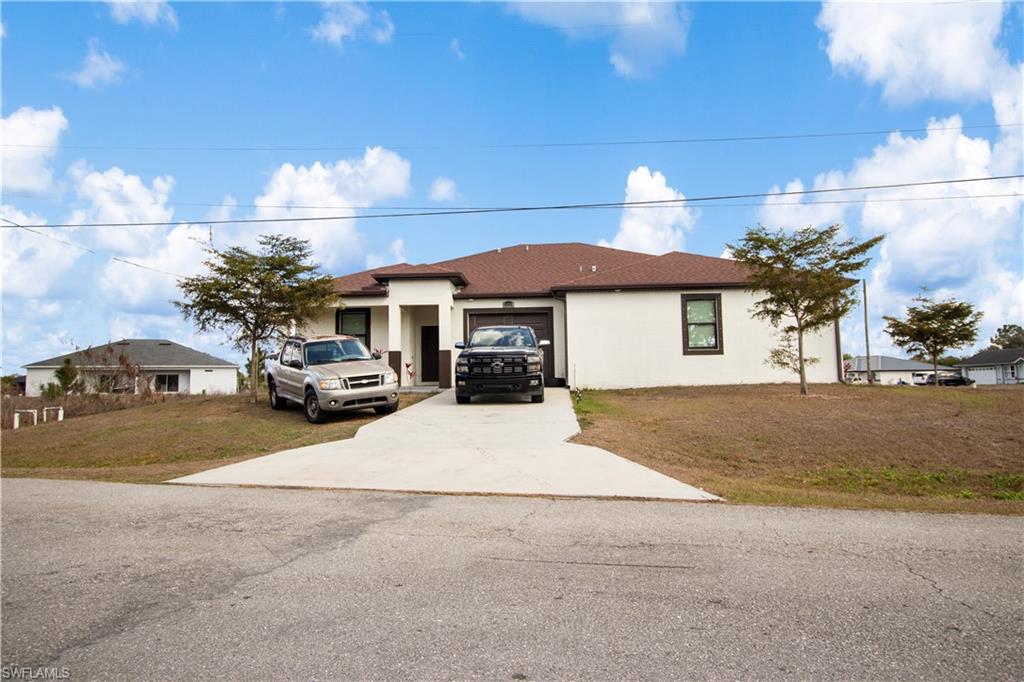 View of front of property featuring a front yard, driveway, stucco siding, and a garage