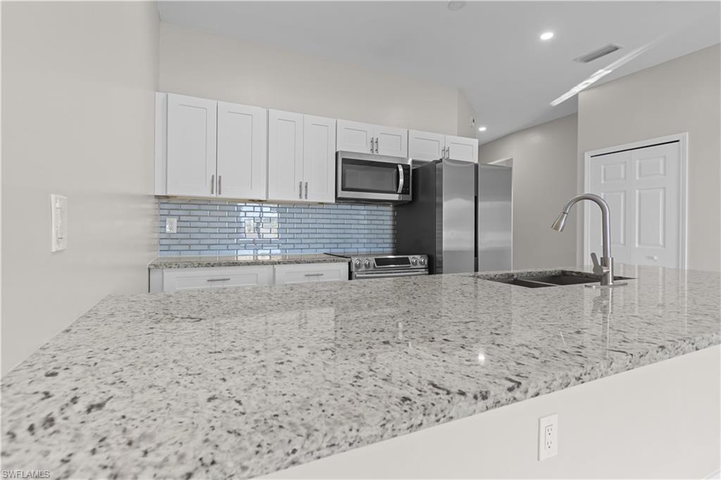 Kitchen with light stone countertops, white cabinetry, stainless steel appliances, and decorative backsplash