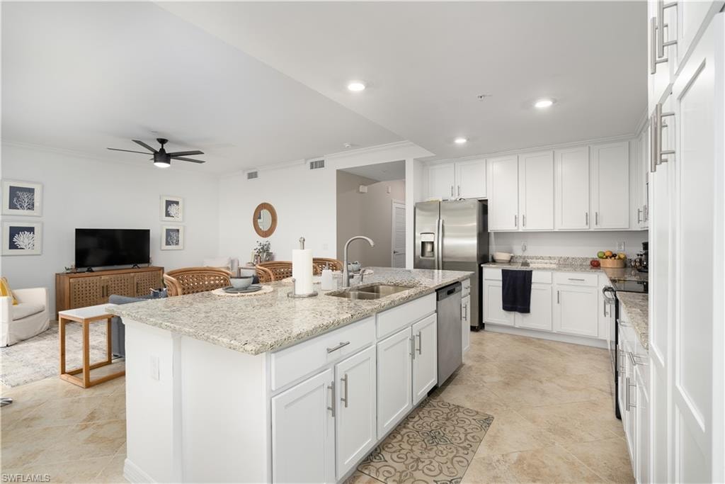 Kitchen with stainless steel appliances, an island with sink, a sink, and white cabinetry