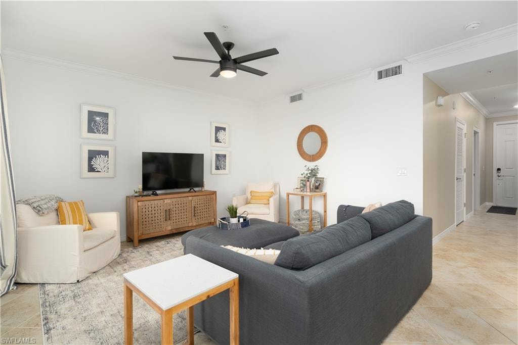 Living room with a ceiling fan, light tile patterned floors, visible vents, and crown molding