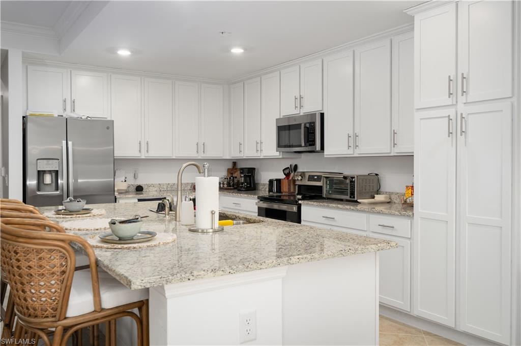Kitchen with crown molding, appliances with stainless steel finishes, white cabinetry, a sink, and an island with sink