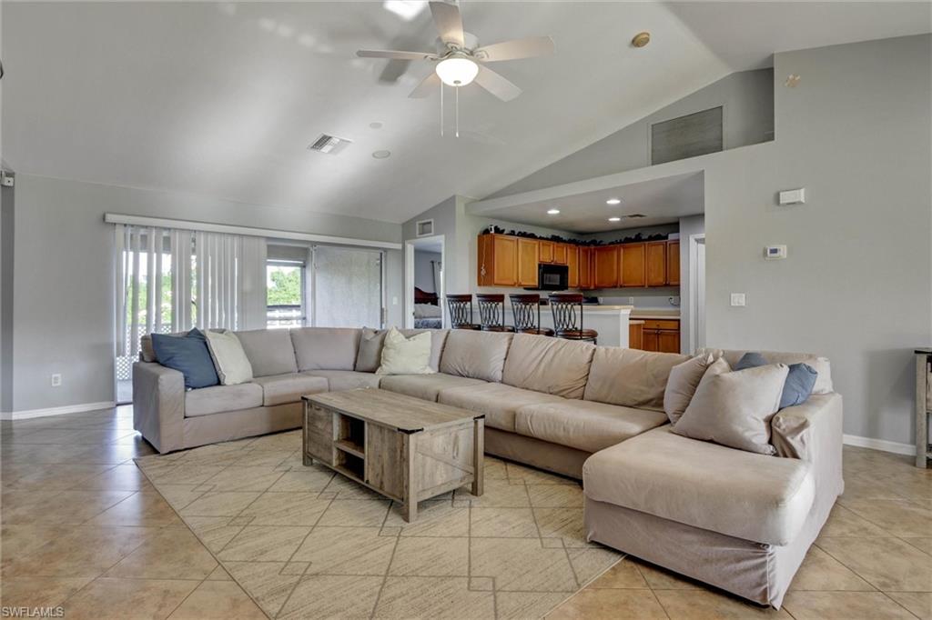 Living room with ceiling fan, light tile patterned flooring, and vaulted ceiling